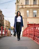 charmante femme réfléchie et habillée à la mode avec de longs cheveux noirs voyage à travers l'europe, marchant dans le centre-ville de st. petersbourg. une belle fille erre seule dans les rues d'automne photo