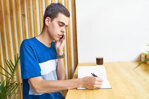 jeune homme écrivant des informations sur le bloc-notes et parlant au téléphone portable, adolescent en vêtements décontractés planifie un horaire