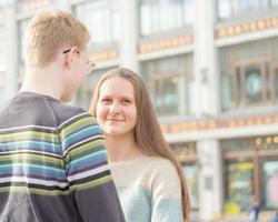 un homme aux cheveux roux embrasse une femme, un garçon dans un pull réconforte une fille aux longs cheveux noirs et épais. concept d'amour chez les adolescentes, relation, couple. ville, front de mer. photo