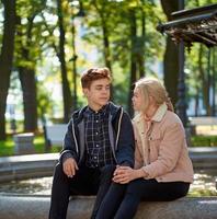 amoureux garçon et fille se regardent, assis dans le parc près de la fontaine à l'automne. petite amie et petit ami parlent concept d'amour et de bonheur photo