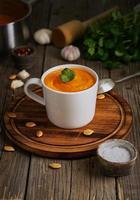 soupe à la crème de pupmkin dans une tasse sur une table en bois marron, verticale, vue latérale. purée végétarienne diététique sur planche à découper avec persil, ail.