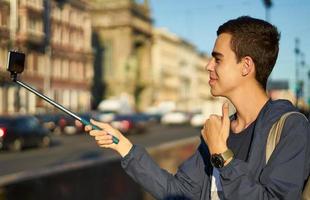 un jeune homme avec un téléphone est dans la rue d'une grande ville et lève le pouce, le blogueur communique avec les gens photo