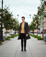 bel homme à la mode élégant, brune en élégant manteau gris, se dresse dans la rue du centre historique de st. petersbourg. jeune homme aux cheveux noirs, sourcils épais. photo