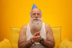 vieil homme positif en chapeau de fête souriant à la caméra, anniversaire photo