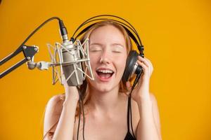 beau visage de femme rousse chantant avec un microphone argenté à condensateur bouche ouverte exécutant la chanson pose sur fond jaune copiez l'espace pour votre texte. animateur radio fm. photo