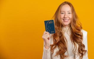 belle fille rousse aux cheveux bouclés en voyage. prochain voyage. fille tenant un passeport brésilien. sur jaune. photo