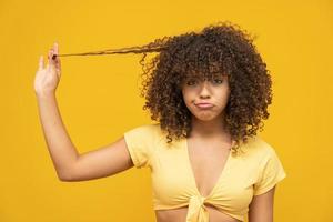 gros plan malheureuse jeune femme frustrée surprise qu'elle perd ses cheveux, recule la racine des cheveux. fond jaune. émotion d'expression du visage humain. concept de coiffure de beauté. fille aux cheveux bouclés. brésilien. photo