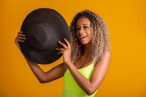 jolie fille aux cheveux bouclés dans un bikini vert vif, un chapeau, une bouche ouverte émotionnellement sur un fond jaune vif avec un corps parfait. isolée. tourné en studio. photo