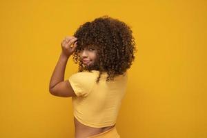 femme africaine américaine à l'envers avec ses cheveux bouclés sur fond jaune. femme bouclée riante en pull touchant ses cheveux et regardant la caméra. photo