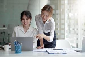 deux jeunes femmes d'affaires asiatiques discutent de la stratégie de travail et de planification du projet d'investissement. gens d'affaires parlant avec un ordinateur portable au bureau. photo