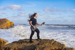 jeune homme aux cheveux noirs et longs jouer de la guitare sur la plage photo