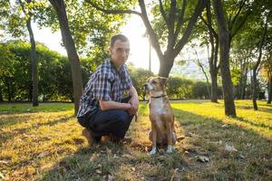 heureux jeune homme jouer avec un chien non de race dans le parc ensoleillé d'été photo