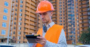 portrait d'un spécialiste de la construction en casque orange et gilet de sécurité contre un grand bâtiment photo