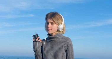 jeune belle femme écouter de la musique avec des écouteurs en plein air sur la plage contre un ciel bleu ensoleillé photo