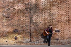 jeune homme aux cheveux longs et tatouage jouer à la guitare acoustique à l'extérieur dans la rue photo