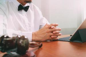 contexte de la justice et du droit. main d'avocat masculin travaillant avec un téléphone intelligent, un clavier d'accueil pour ordinateur tablette numérique avec un marteau et un document sur une table en bois photo