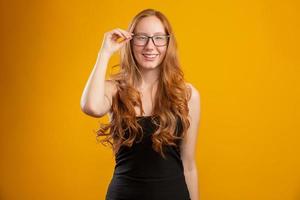 belle jeune femme rousse aux cheveux bouclés heureuse avec ses lunettes. concept de soins oculaires. sur fond jaune. photo