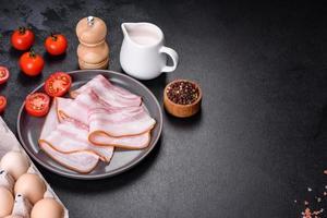 délicieux bacon cru frais coupé avec des tranches sur une plaque grise sur un fond de béton foncé