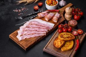 tranches de délicieux bacon cru ou salé avec épices, sel, légumes et herbes sur une planche à découper en bois