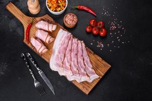 tranches de délicieux bacon cru ou salé avec épices, sel, légumes et herbes sur une planche à découper en bois