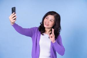 portrait d'une femme asiatique d'âge moyen utilisant un smartphone sur fond bleu photo