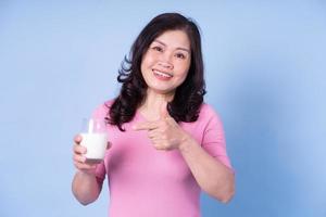 image d'une femme asiatique d'âge moyen buvant du lait sur fond bleu photo