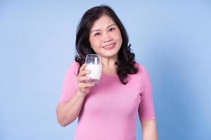 image d'une femme asiatique d'âge moyen buvant du lait sur fond bleu photo