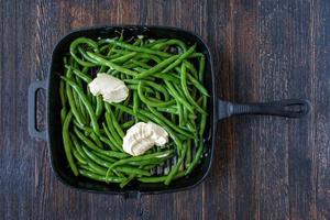 Haricots verts entiers frais de la ferme avec du beurre à plat en fonte photo