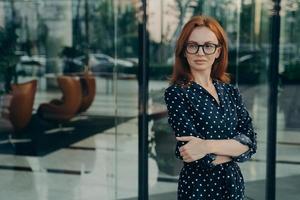 une réalisatrice sûre d'elle aux cheveux rouges pose près d'un immeuble de bureaux photo