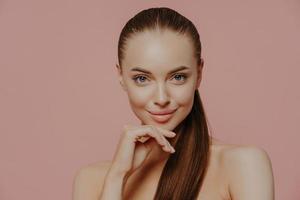 soins de la peau et procédures anti-âge. une jeune femme brune confiante garde la main sous le menton, a les cheveux peignés, une peau propre et fraîche, bénéficie de soins de beauté, pose avec un corps nu sur fond rose photo