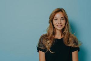 femme aux cheveux longs regarde directement la caméra avec une expression tendre vêtue d'un t-shirt noir décontracté photo