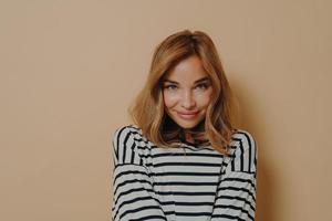 jeune femme charmante aux cheveux blonds teints en chemise rayée regardant la caméra avec un sourire timide photo