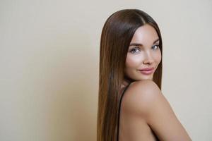 séduisante jeune femme européenne avec une peau douce et saine, un corps parfait, semble calme directement à la caméra, a les cheveux longs, se tient à l'intérieur sur fond beige. concept jeunesse, beauté et soins de la peau. photo