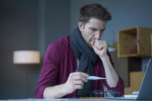 entrepreneur masculin à l'air malsain en écharpe autour du cou toussant regarde un thermomètre numérique photo