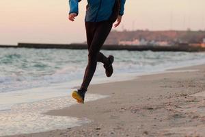 jeune homme en vêtements d'automne s'entraînant sur la plage, fond de lever de soleil, coureur masculin le matin photo