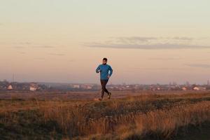 jeune homme trail runner s'entraînant à l'extérieur dans les champs, coucher de soleil sur fond de lac photo