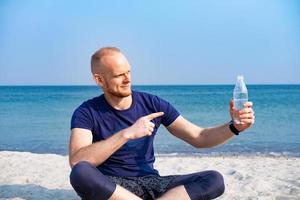 jeune athlète masculin buvant de l'eau douce à partir d'une bouteille en plastique sur la plage photo