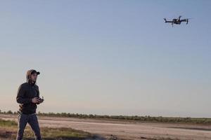 photo d'un drone quadrocopter écorchant noir et d'une siluette pilote sur fond clair au coucher du soleil, l'hélicoptère dron utilisé par les touristes pour photographier ou filmer des paysages désertiques