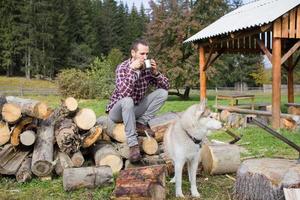 touriste se reposant sur le bois haché avec un chien husky et buvant du thé ou du café photo