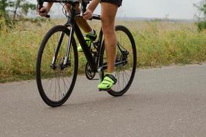 coureur cycliste en casque et vêtements de sport s'entraînant seul sur une route de campagne vide, des champs et des arbres sur fond photo