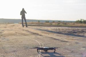 photo d'un drone quadrocopter écorchant noir et d'une siluette pilote sur fond clair au coucher du soleil, l'hélicoptère dron utilisé par les touristes pour photographier ou filmer des paysages désertiques