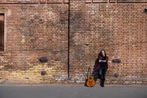 jeune homme aux cheveux longs et tatouage jouer à la guitare acoustique à l'extérieur dans la rue photo