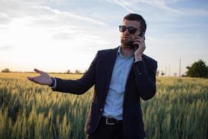 homme d'affaires dans les champs de blé d'été à l'aide d'une tablette pendant le coucher du soleil, homme en costume avec ordinateur compact photo