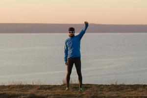 jeune homme trail runner s'entraînant à l'extérieur dans les champs, coucher de soleil sur fond de lac photo