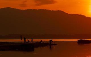 beau ciel de lever de soleil au-dessus de la montagne au réservoir. les gens pêchent avec une canne à pêche sur la rivière. paysage de réservoir et de montagne avec un ciel de lever de soleil orange. silhouette vie le matin. photo