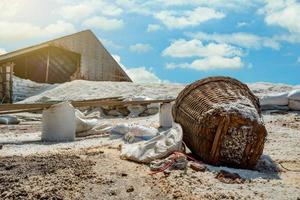 grange avec du sel de saumure dans le sac. tas de sel de mer bio et panier de bambou devant la grange avec ciel bleu et nuages blancs en été. matière première du sel industriel. sel de mer dans un sac en plastique. photo