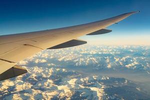 aile d'avion au-dessus de la couverture de montagne avec de la neige blanche. avion volant sur le ciel bleu. vue panoramique depuis la fenêtre de l'avion. vol d'une compagnie aérienne commerciale. aile d'avion. concept de mécanique de vol. vol international. photo