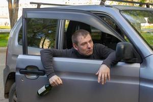 conducteur ivre avec une bouteille d'alcool tombe par la porte de sa propre voiture photo