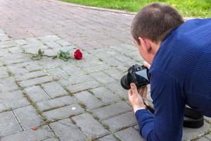photographe prend des photos d'une rose rouge allongée sur un trottoir