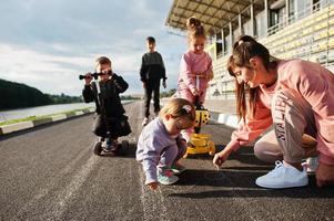 jeune mère élégante avec quatre enfants en plein air. la famille sportive passe du temps libre à l'extérieur avec des scooters et des patins. photo